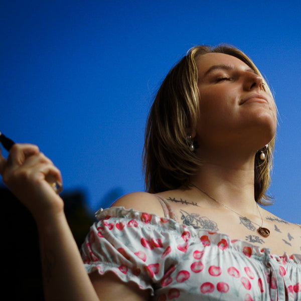 Woman with tattoos wearing a floral off-shoulder top against a blue sky.