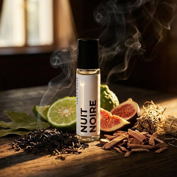 Nuit Noire perfume oil bottle with smoke on a wooden surface with limes, figs, and herbs. long lasting perfume oil, vegan and cruelty-free by JYCTY